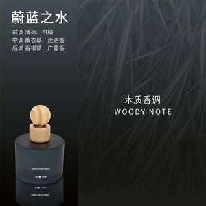 A dark cylindrical car perfume bottle with a light wood cap and spherical topper, shown on a dark textured background with Chinese and English text reading 'WOODY NOTE'.