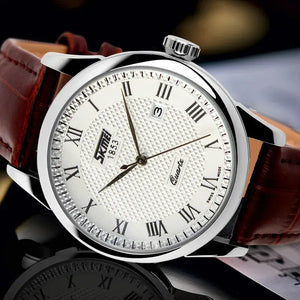A close-up of a SKMEI wristwatch with a silver-toned round case, white textured dial, Roman numeral hour markers, a date window, and a brown leather strap.