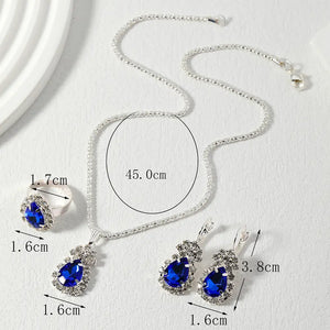 Silver-tone jewelry set with a necklace, ring, and earrings featuring deep blue teardrop-shaped crystals, shown with measurement labels on a light textured background.